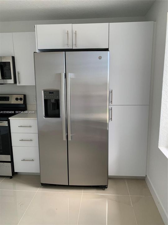 Stainless steel side-by-side refrigerator, white flat-panel cabinetry, light-toned tile flooring, and integrated built-in pantry storage