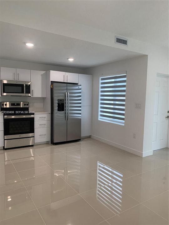 Kitchen featuring white cabinetry, stainless steel appliances, large-format tile flooring, and a window with motorized zebra blinds