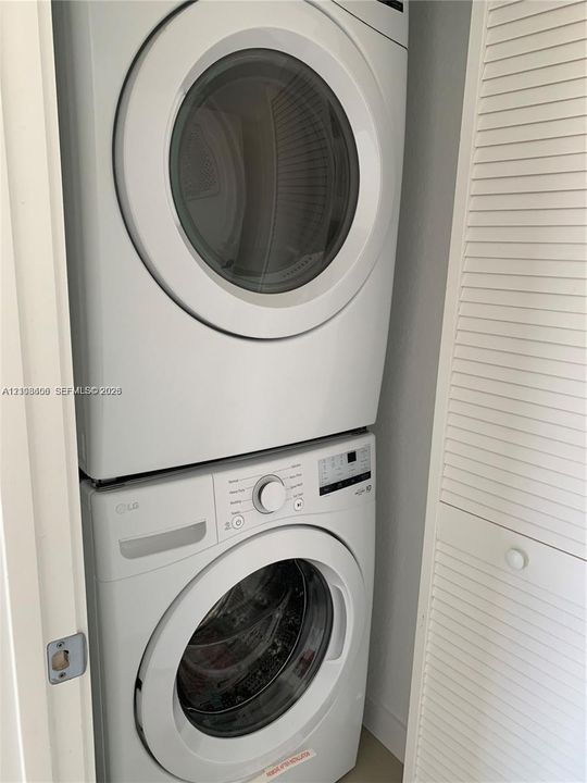 Stacked white front-load washer and dryer unit enclosed by bi-fold louvered doors