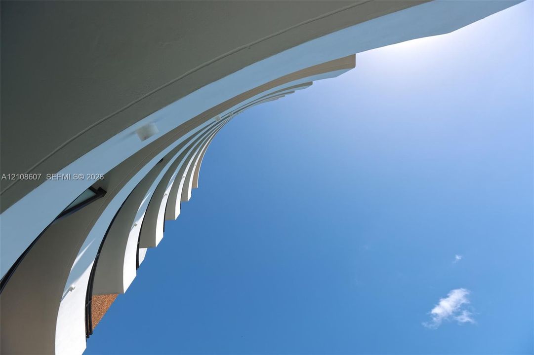 Curved architectural facade featuring clean lines, structural concrete fin detailing, and integrated exterior lighting
