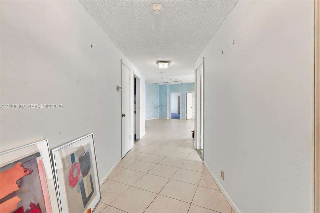 Interior hallway featuring neutral-toned tile flooring, multi-panel interior doors, and overhead light fixtures