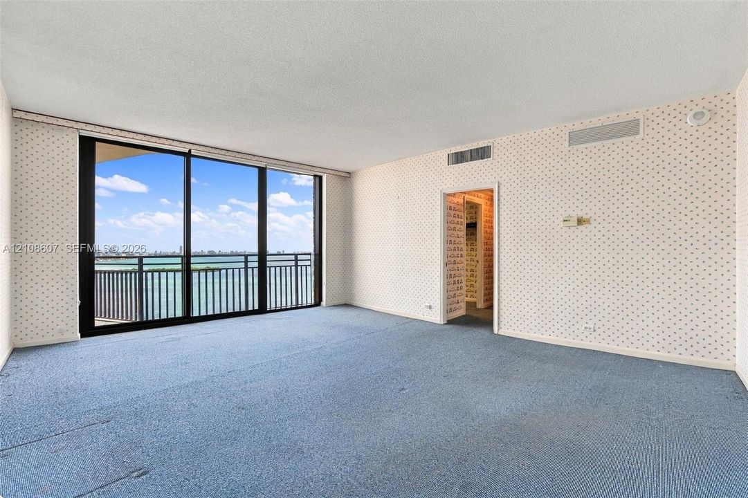 Floor-to-ceiling glass sliding doors opening to a private balcony with water frontage, wall-to-wall carpeting, and neutral textured wallcoverings