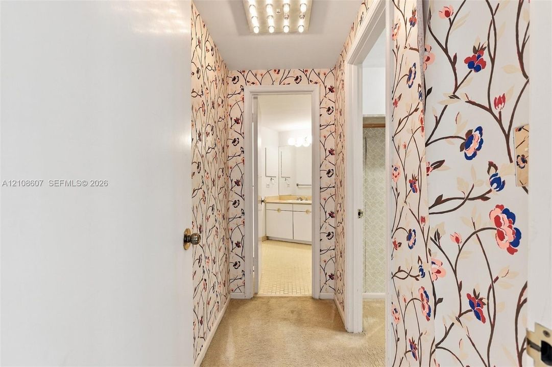 Hallway featuring floral-patterned wallpaper, flush-mount lighting, and solid-core interior doors with metallic hardware