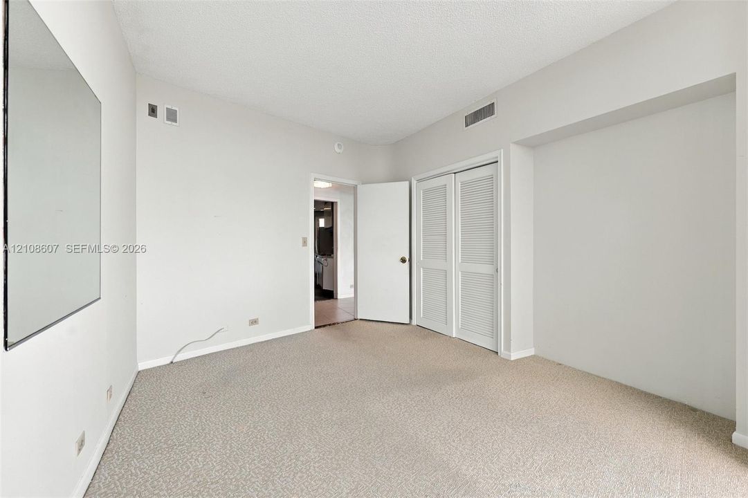 Room featuring neutral wall-to-wall carpeting, a large wall-mounted mirror, and a double-door closet with louvered panels