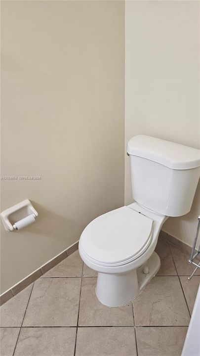 White ceramic toilet with an attached wall-mounted paper holder and neutral-toned diagonal tile flooring