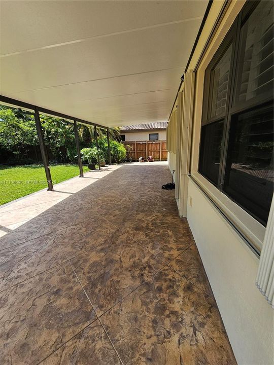 Covered patio featuring stamped concrete flooring, support columns, and access to a fenced yard