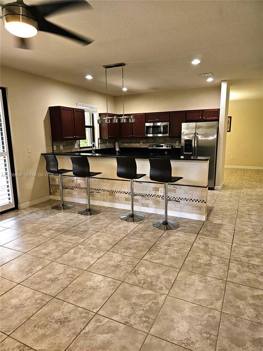Kitchen featuring dark wood cabinetry, stainless steel appliances, black countertops, decorative stone-tile backsplash, and large-format tile flooring