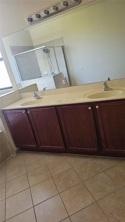 Double vanity featuring dark wood cabinetry, solid surface countertop with integrated dual sinks, large wall-mounted mirror, and ceramic tile flooring