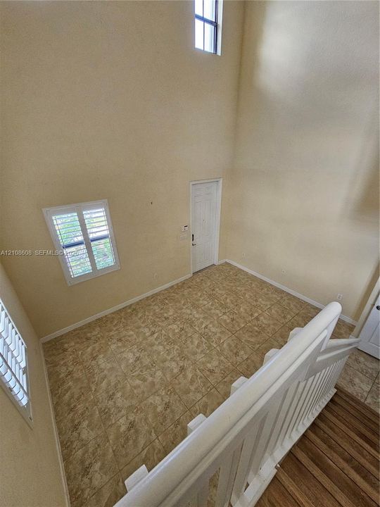 Double-height ceiling featuring tall vertical windows, tile flooring, and a white wood-finish staircase railing