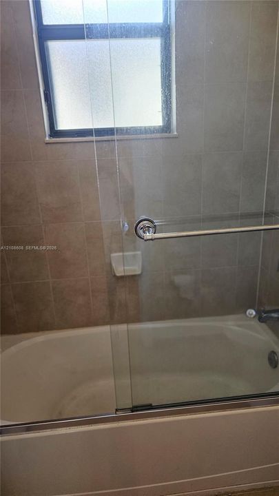 Bathtub with a glass sliding enclosure, integrated soap dish, and neutral wall tile surround