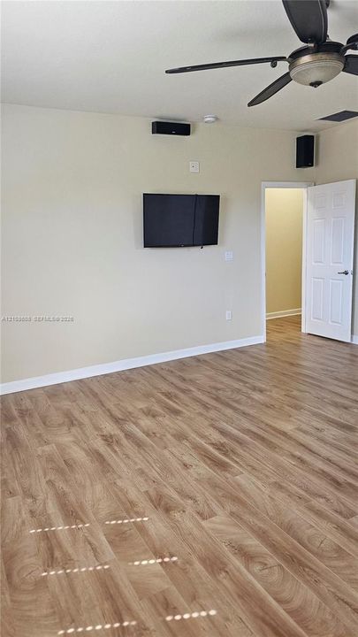 Wood-finish flooring, ceiling fan with integrated lighting, wall-mounted display hardware, and a paneled interior door