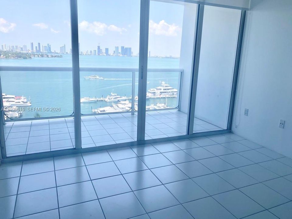 Floor-to-ceiling sliding glass doors, white ceramic tile flooring, and a private balcony featuring a glass railing