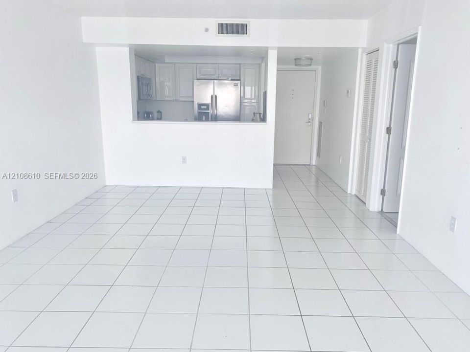 Open-concept interior featuring white ceramic floor tiling, white cabinetry, stainless steel kitchen appliances, and bi-fold closet doors