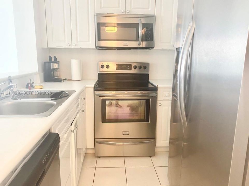 Kitchen featuring white cabinetry, stainless steel appliances, a glass-top electric range, a built-in microwave, and tile flooring