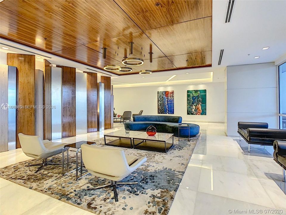 Interior space featuring a high-gloss wood-paneled ceiling, large-format stone flooring, integrated recessed lighting, metallic wall paneling, and contemporary circular pendant light fixtures