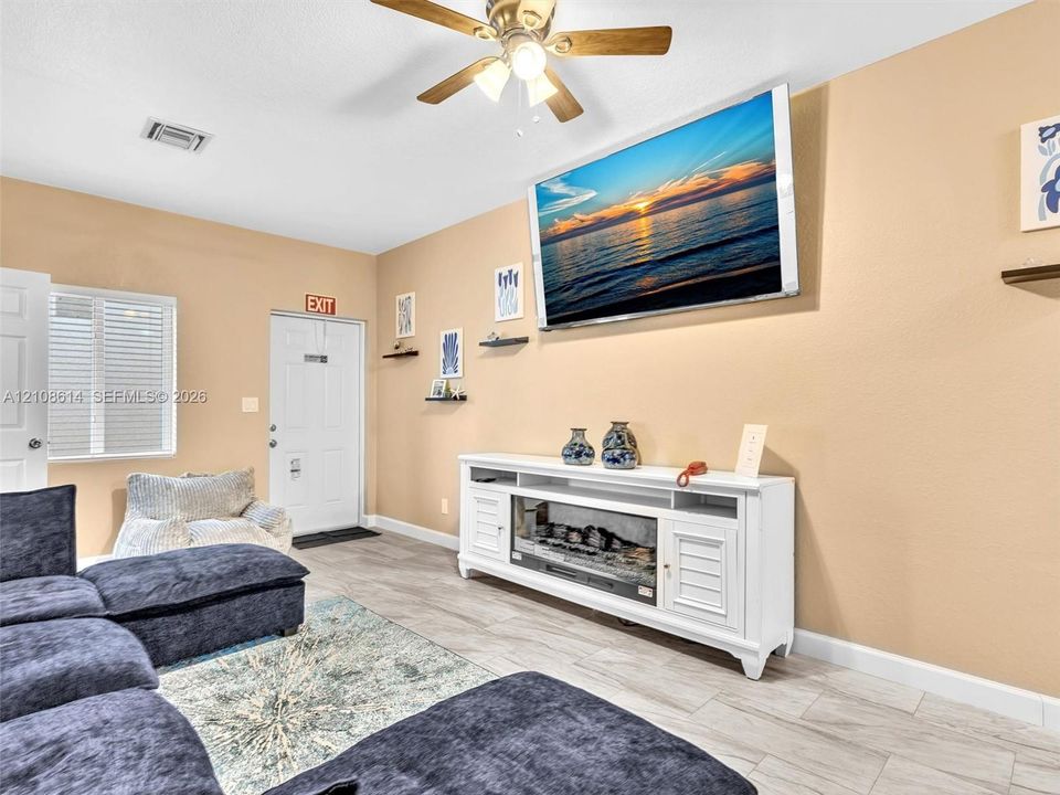 Neutral-toned interior space featuring wood-finish flooring, a ceiling fan with integrated lighting, and a white built-in media console with an electric fireplace