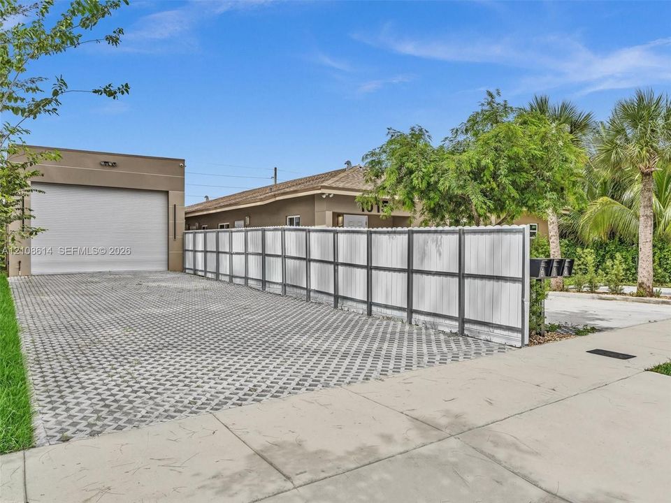 Exterior featuring a detached garage with roll-up door, paved permeable driveway, and full-height privacy fencing