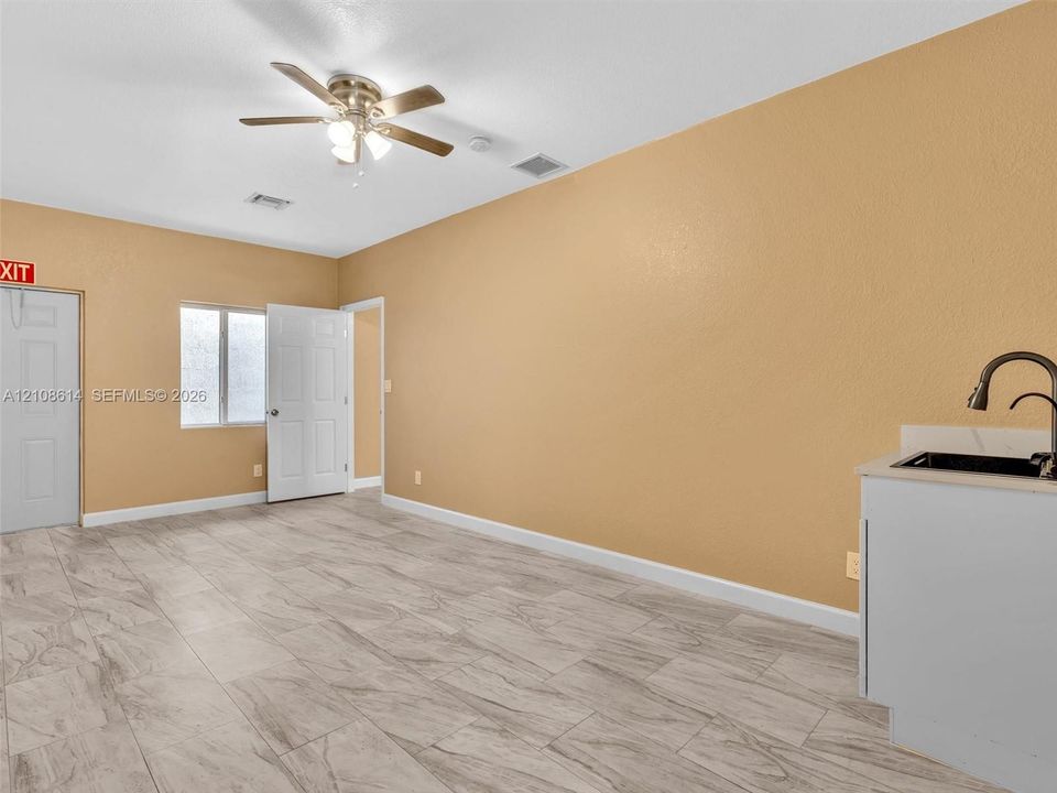 Tile flooring with a wood-grain finish, white cabinetry with a light-toned countertop, integrated sink with a gooseneck faucet, ceiling fan, and window with textured privacy glass