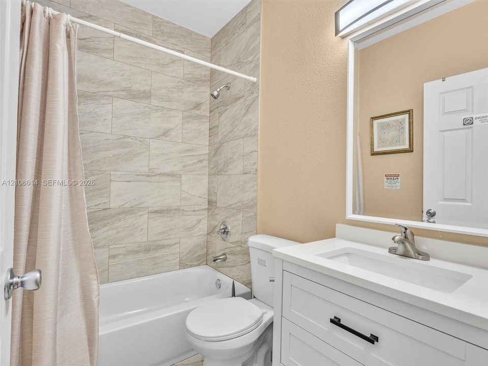 Bathroom featuring a white vanity with an integrated basin, neutral tile-surround tub, modern brushed-nickel fixtures, and a framed mirror with integrated lighting
