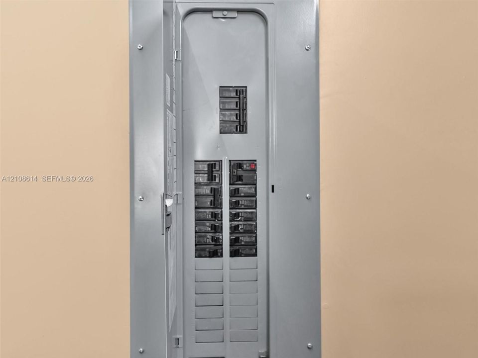 Recessed electrical service panel featuring a metal enclosure with a hinged door and labeled circuit breaker switches