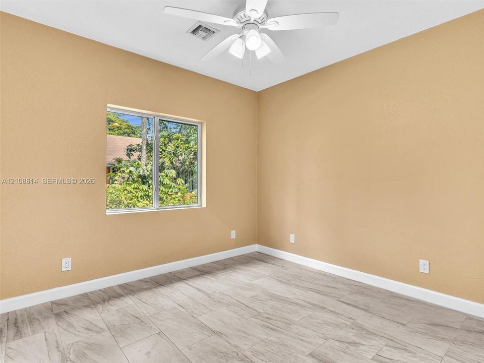 Neutral-toned interior space featuring wood-finish tile flooring, a multi-blade ceiling fan with integrated lighting, and a single-pane window