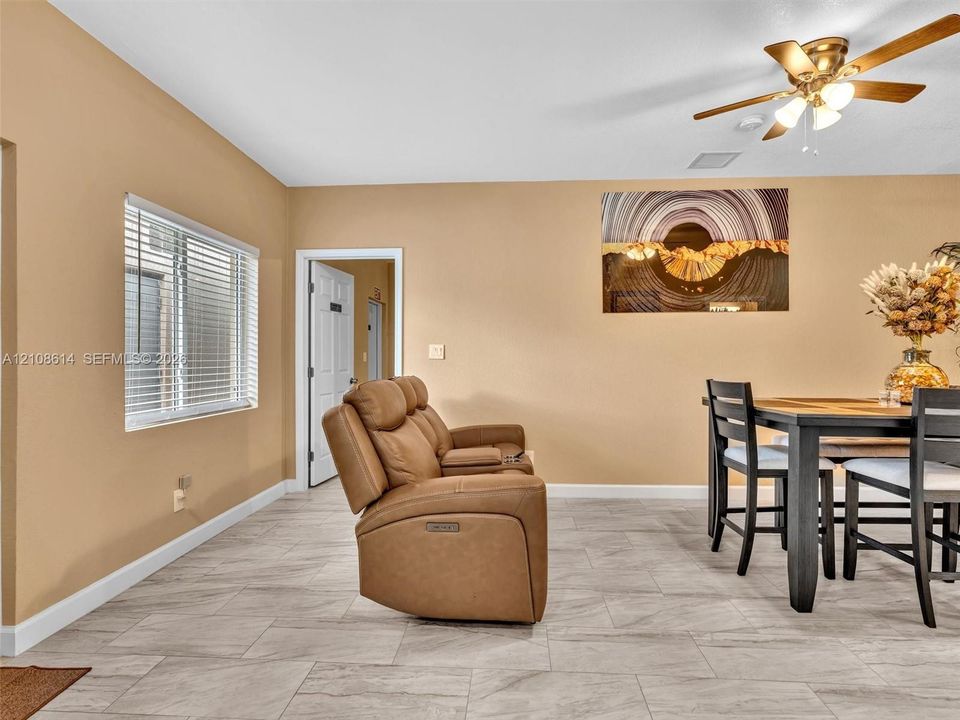 Neutral-toned interior space featuring light-colored stone-finish flooring, a multi-blade ceiling fan with integrated lighting, and a white-framed window with horizontal blinds