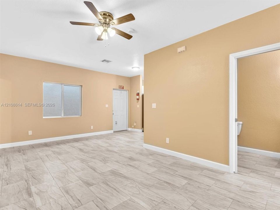 Neutral-toned interior featuring wood-finish tile flooring, a multi-blade ceiling fan with integrated light fixture, and a single-hung window with frosted glass