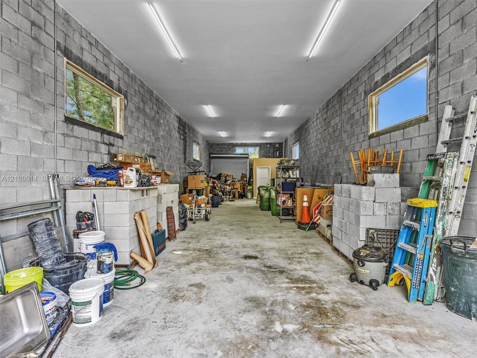 Spacious garage featuring exposed concrete block walls, high-clearance ceilings, concrete flooring, multiple horizontal-slider windows, and linear LED lighting