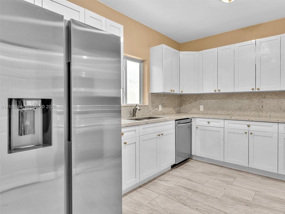 Kitchen featuring white shaker-style cabinetry, stainless steel appliances, speckled stone countertops, and wood-finish tile flooring