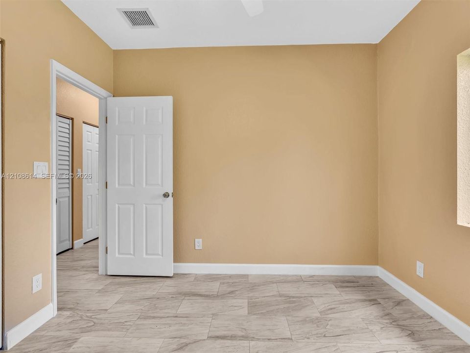 Neutral-toned interior space featuring stone-finish tile flooring, solid-core interior doors, and closet doors with louvered panels