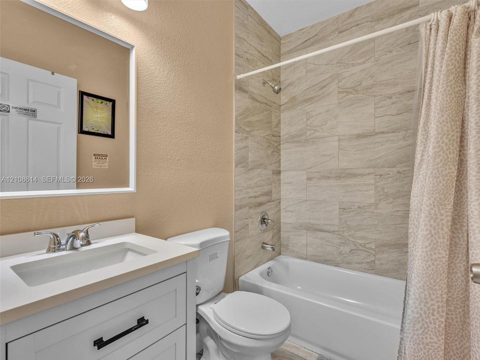 Bathroom featuring a white vanity with a rectangular basin, stone-finish countertop, frameless mirror, and shower-tub combination with horizontal wall tiling