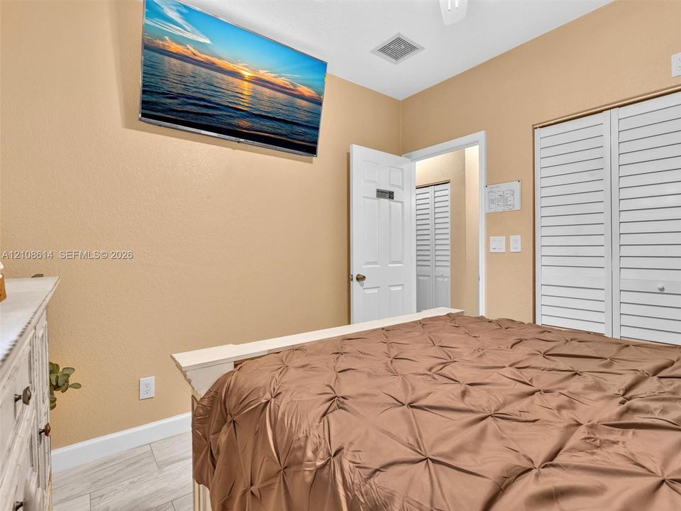 Light-toned wood-finish flooring, white louvered closet doors, and a solid-core interior door with a brushed nickel lever