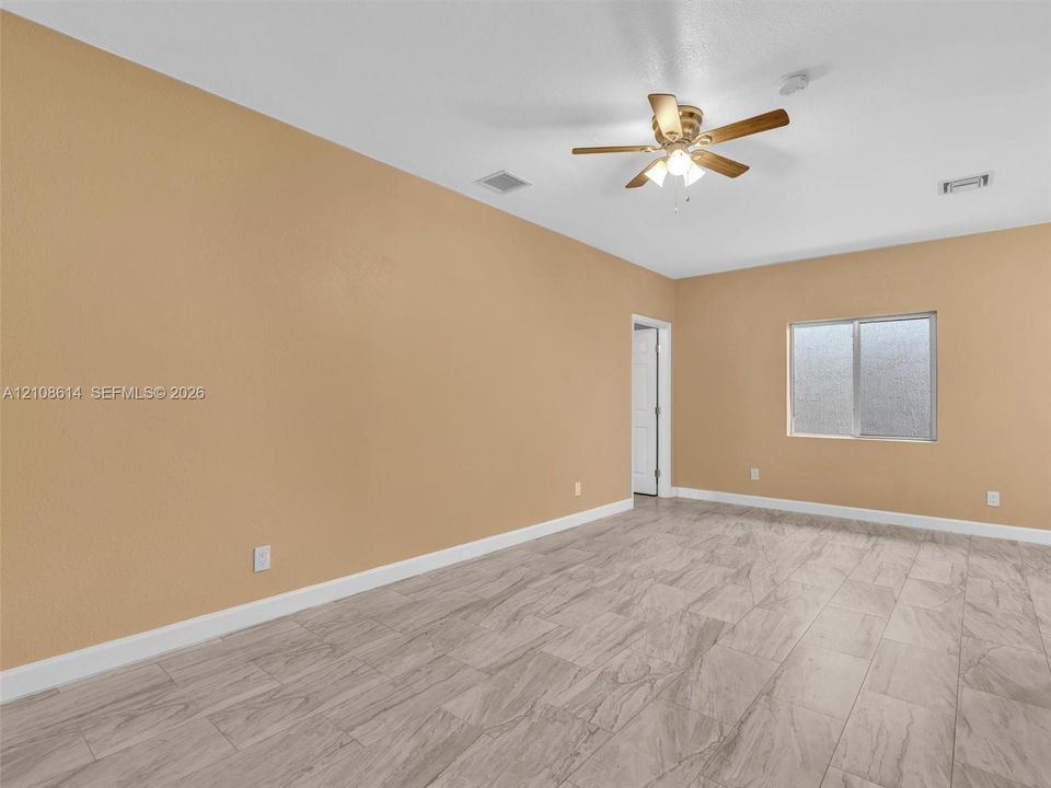 Neutral-toned interior space featuring stone-finish tile flooring, a multi-blade ceiling fan with integrated lighting, and a single-pane sliding window