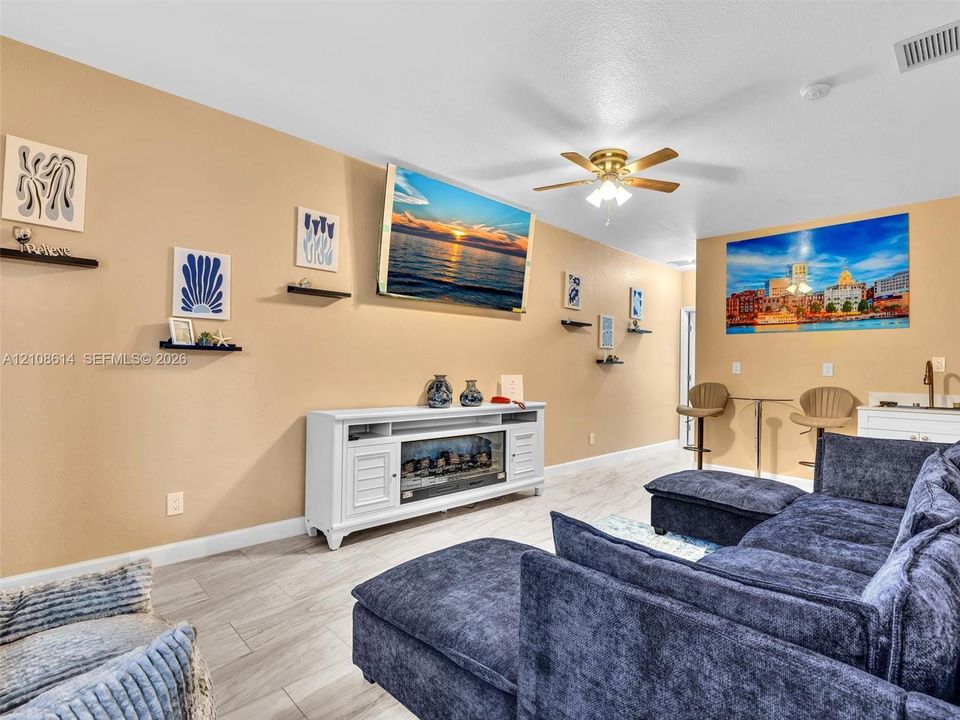 Neutral wall tones, wood-finish flooring, ceiling fan with integrated lighting, and white cabinetry featuring an electric fireplace insert