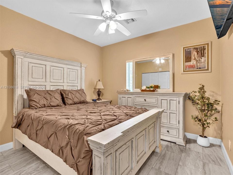 Neutral-toned bedroom featuring wood-finish tile flooring, ceiling fan with integrated lighting, and plantation shutters