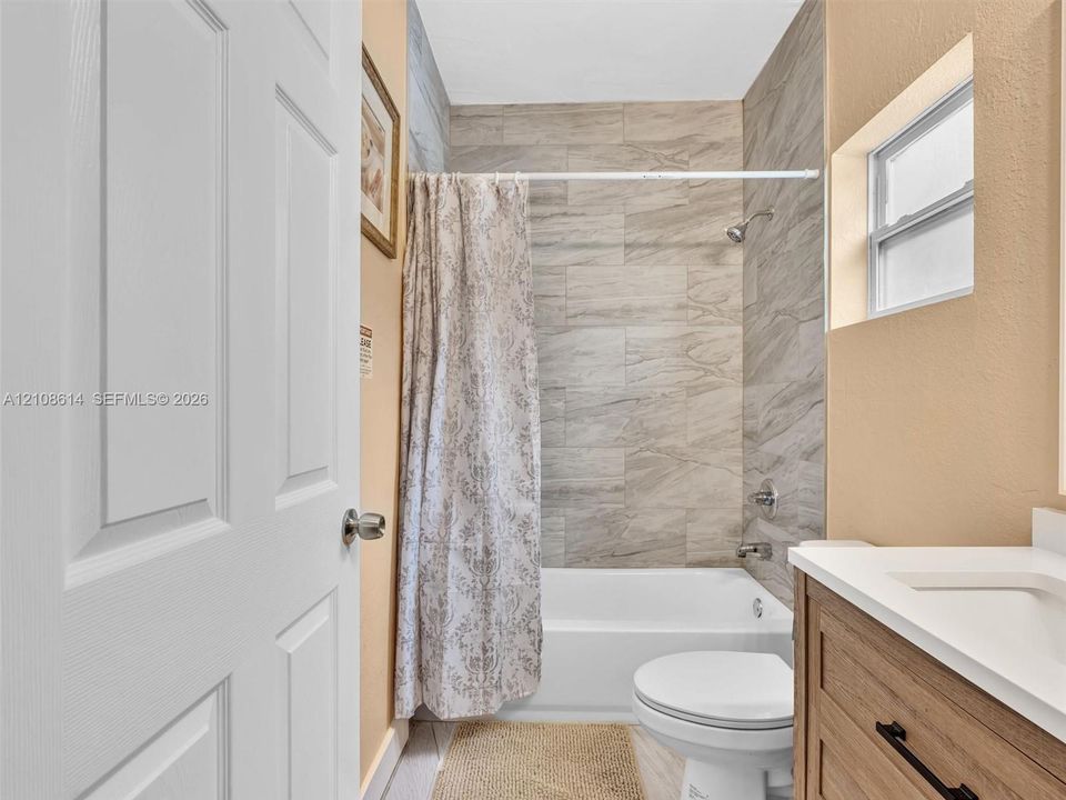 Bathroom featuring a vanity with a light wood-finish cabinet, white countertop, integrated sink, and polished chrome fixtures, accented by neutral-toned tiled shower walls and a bathtub