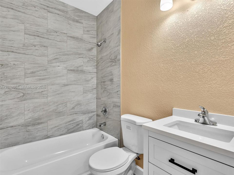 White vanity with a rectangular sink, chrome faucet, and matte black hardware, paired with a bathtub surround featuring large-format grey tile