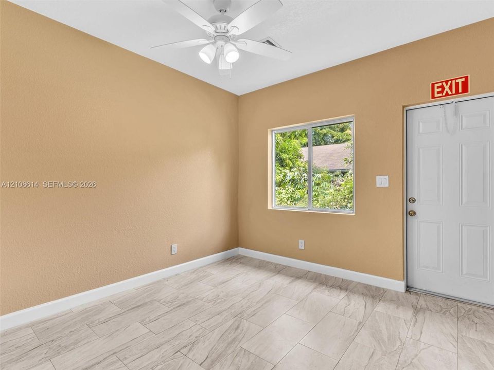 Interior room featuring neutral-toned walls, tile flooring with a stone-finish pattern, a white ceiling fan with integrated lighting, and a single-pane sliding window