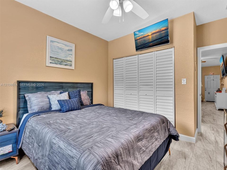 Room featuring four-panel louvered closet doors, neutral wall finish, and white ceiling fan with integrated lighting