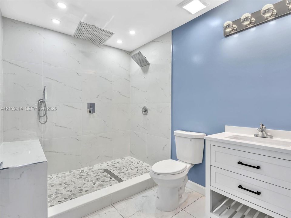 Walk-in shower featuring large-format tile walls, a pebble-stone floor, and a rainfall showerhead, complemented by a white vanity with integrated basin and polished chrome fixtures