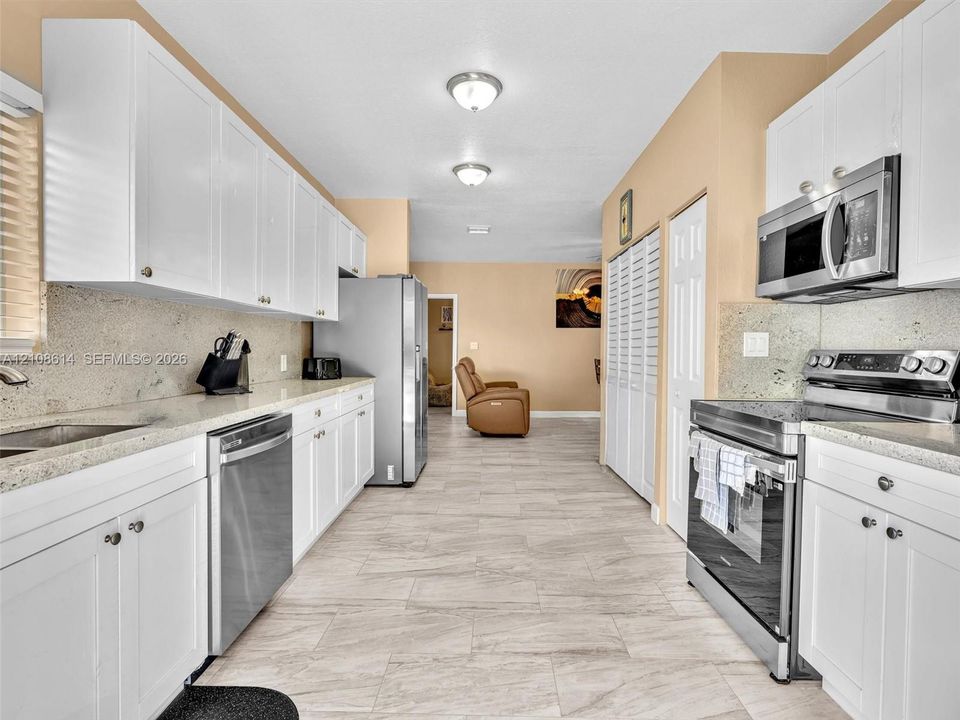 Kitchen featuring white shaker-style cabinetry, stone-finish countertops, stainless steel appliances, and tile flooring