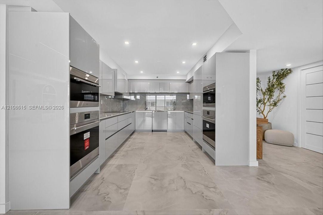 Contemporary kitchen featuring high-gloss cabinetry, built-in stainless steel double ovens, integrated appliances, and large-format tile flooring with recessed lighting
