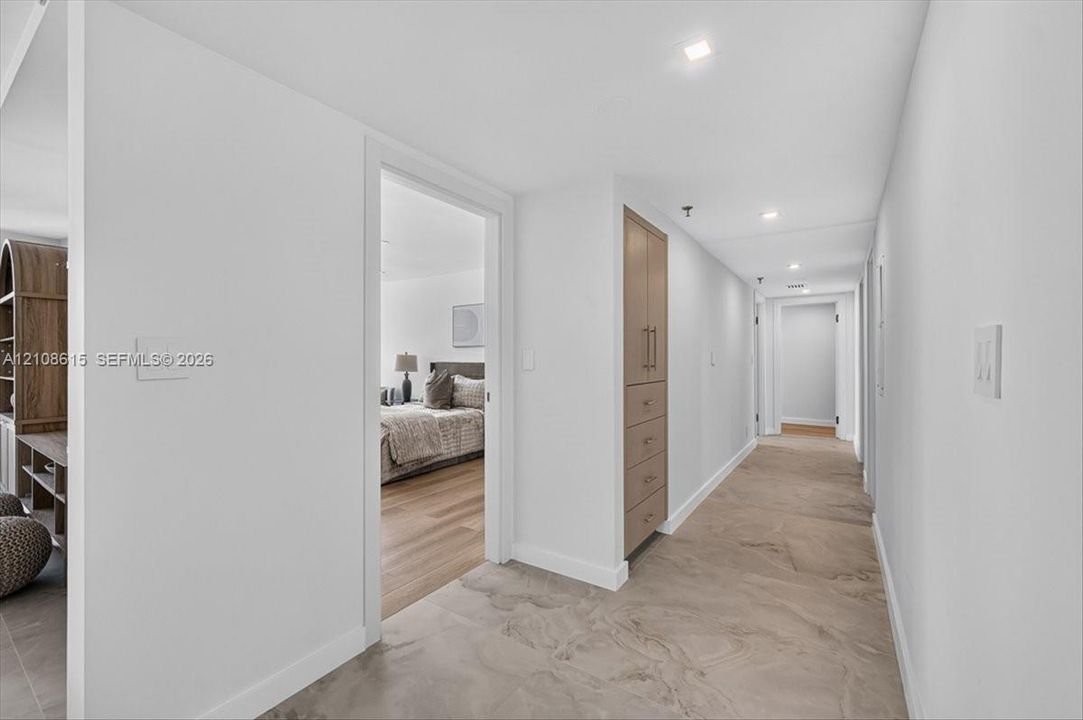 Hallway featuring large-format tile flooring, recessed ceiling lighting, and built-in floor-to-ceiling cabinetry with wood-finish doors