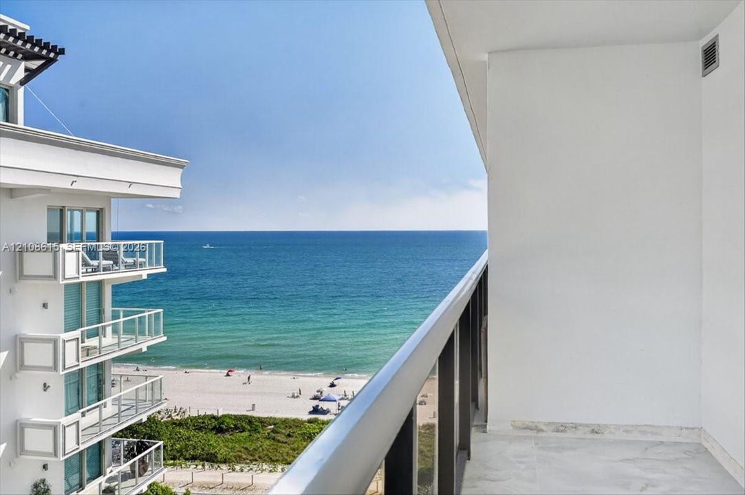 Private balcony with stone flooring and a glass-paneled railing overlooking the ocean and coastline