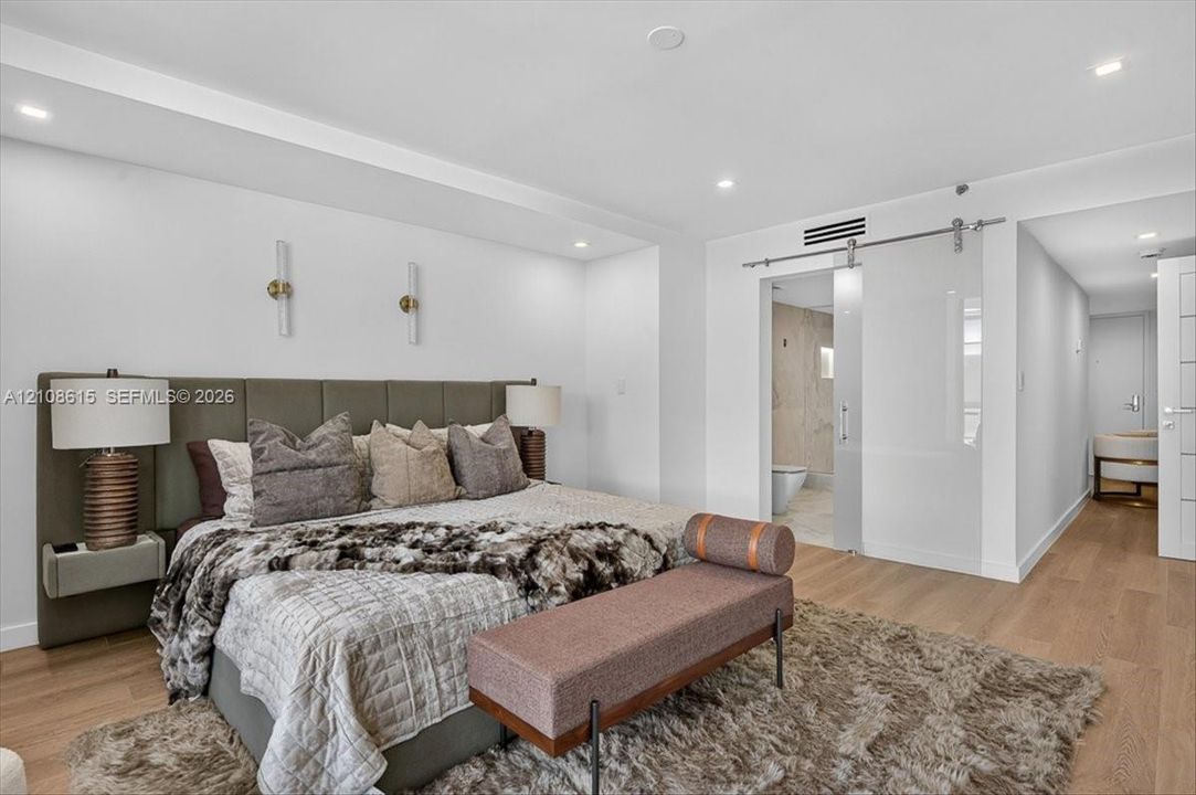 Wood-finish flooring, recessed lighting, wall-mounted light fixtures, and a glass sliding barn door with brushed metal hardware