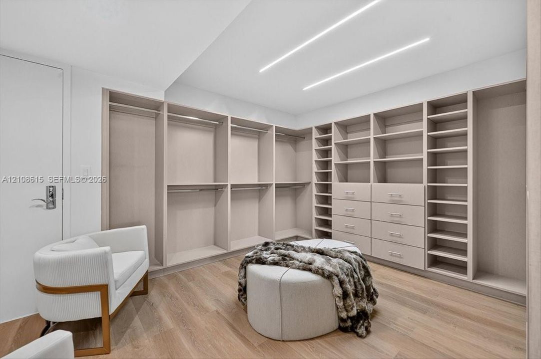 Custom reach-in closet featuring light wood-finish shelving, integrated drawers with hardware, wood-finish flooring, and recessed linear ceiling lighting