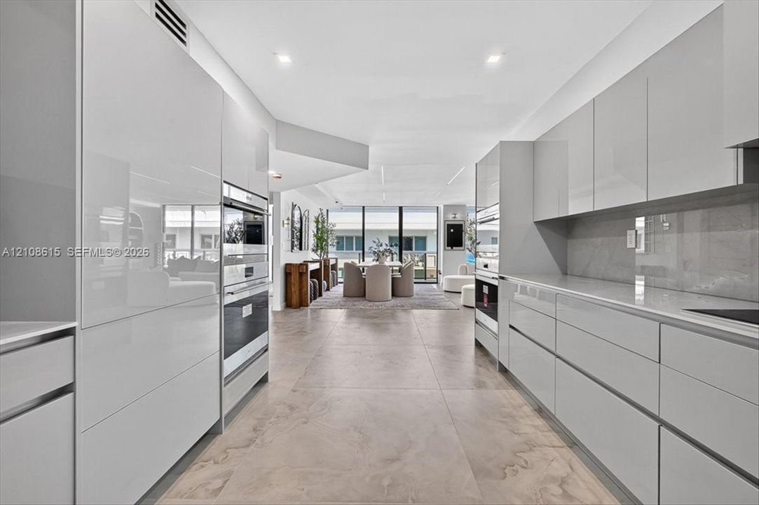Contemporary kitchen featuring high-gloss cabinetry, large-format tile flooring, stone-surfaced countertops, and built-in stainless steel double ovens