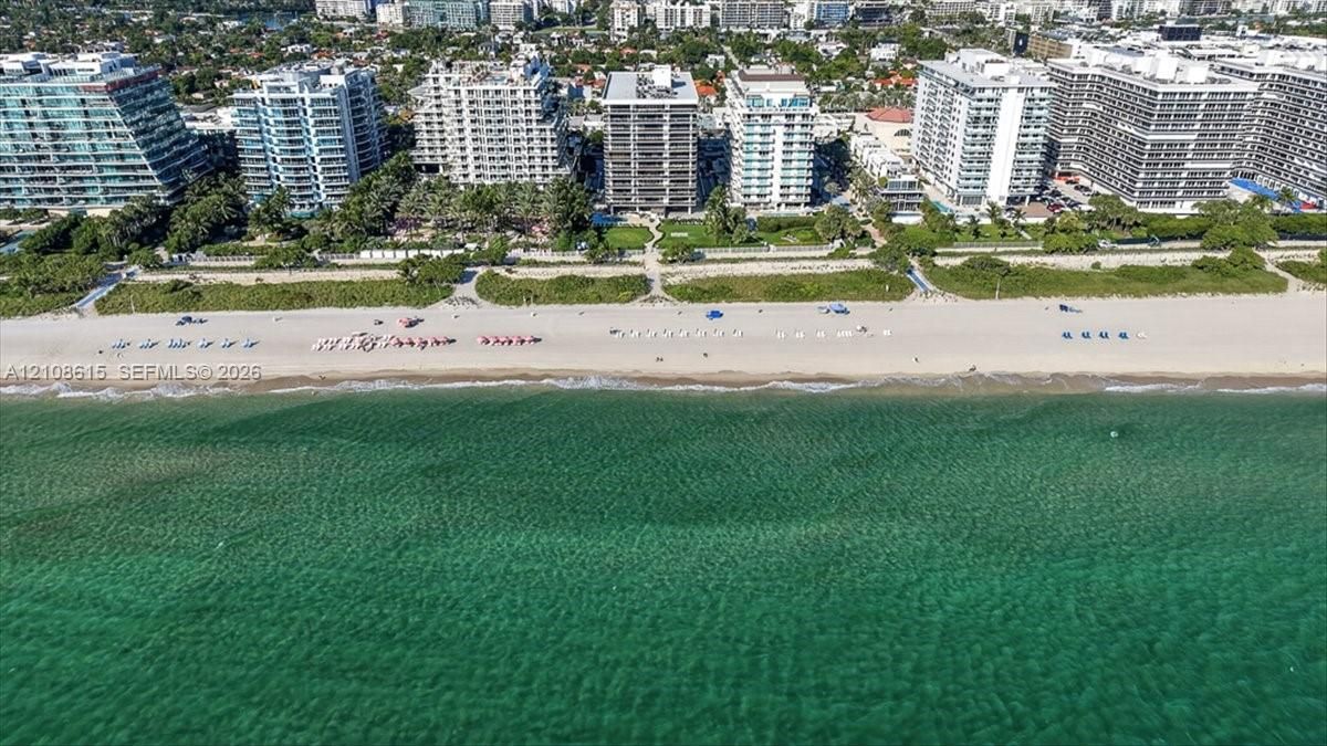 Aerial perspective of beachfront property featuring direct sand access, paved walkways, landscaped grounds, and coastal waters