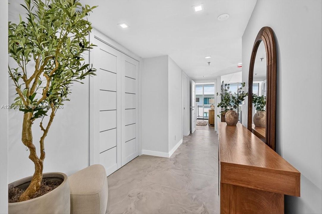 Hallway featuring light-toned smooth-finish flooring, recessed ceiling lighting, and crisp white walls with modern multi-panel interior doors