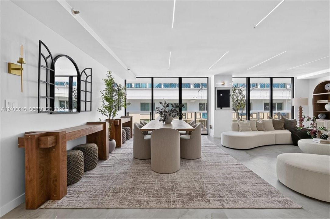 Open-concept space featuring floor-to-ceiling black-framed windows, integrated recessed linear ceiling lighting, light-toned stone-finish flooring, and a built-in arched wooden shelving unit